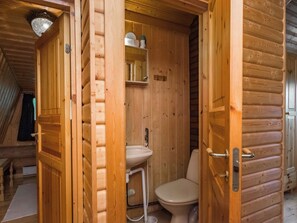 A wooden cabin interior with a wooden door, a toilet, a sink, and a mirror. - Rasilinna by Interhome (Mikkeli)