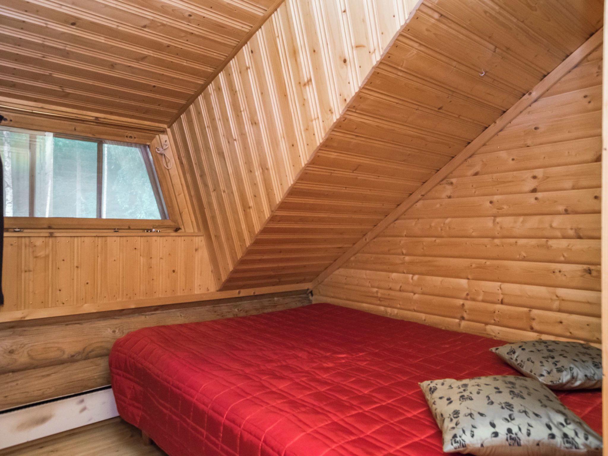 A small, sloped-roofed room with a single bed, a window, and wooden walls.