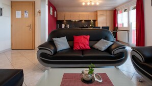 A modern living room with a black sofa, a small coffee table with a plant, and a kitchen in the background.