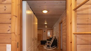Un pasillo de madera con una mecedora y un banco, que conduce a una habitación con una puerta y un reloj de pared.