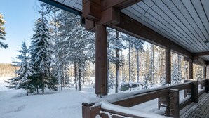 Una terraza cubierta de madera con barandilla nevada, con vistas a un bosque cubierto de nieve.