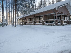 A wooden lodge with a covered porch and a snow-covered roof, surrounded by trees.