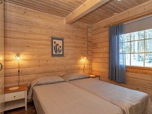 Een kamer in chaletstijl met twee bedden, houten wanden, een raam met gordijnen en een wandlamp.