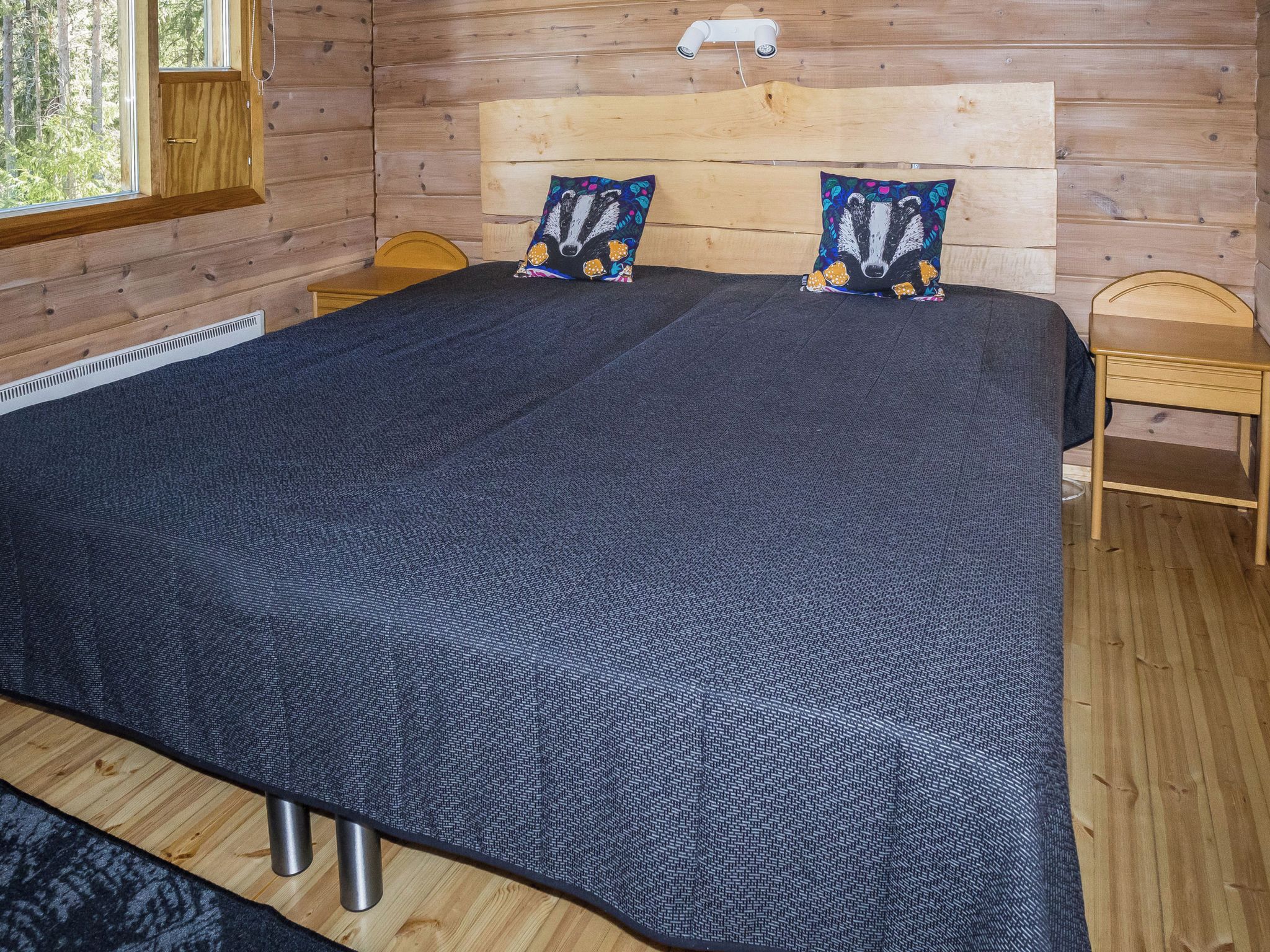 Ein Zimmer einer Holzhütte mit einem großen Bett, zwei Kissen, einem Nachttisch und einem Fenster.