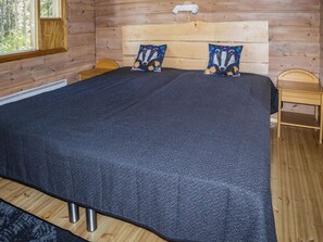 A wooden cabin room with a large bed, two pillows, a nightstand, and a window.