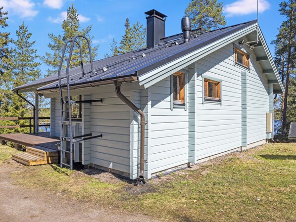 Une maison de plain-pied avec un toit en pente, une cheminée et une terrasse dotée d’un banc.