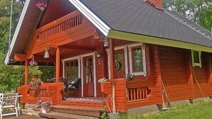 A red wooden house with a porch, a chimney, and a small garden area.