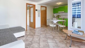 Una sala moderna con sofá, una zona de comedor con mesa y sillas, y una cocina con armarios verdes.