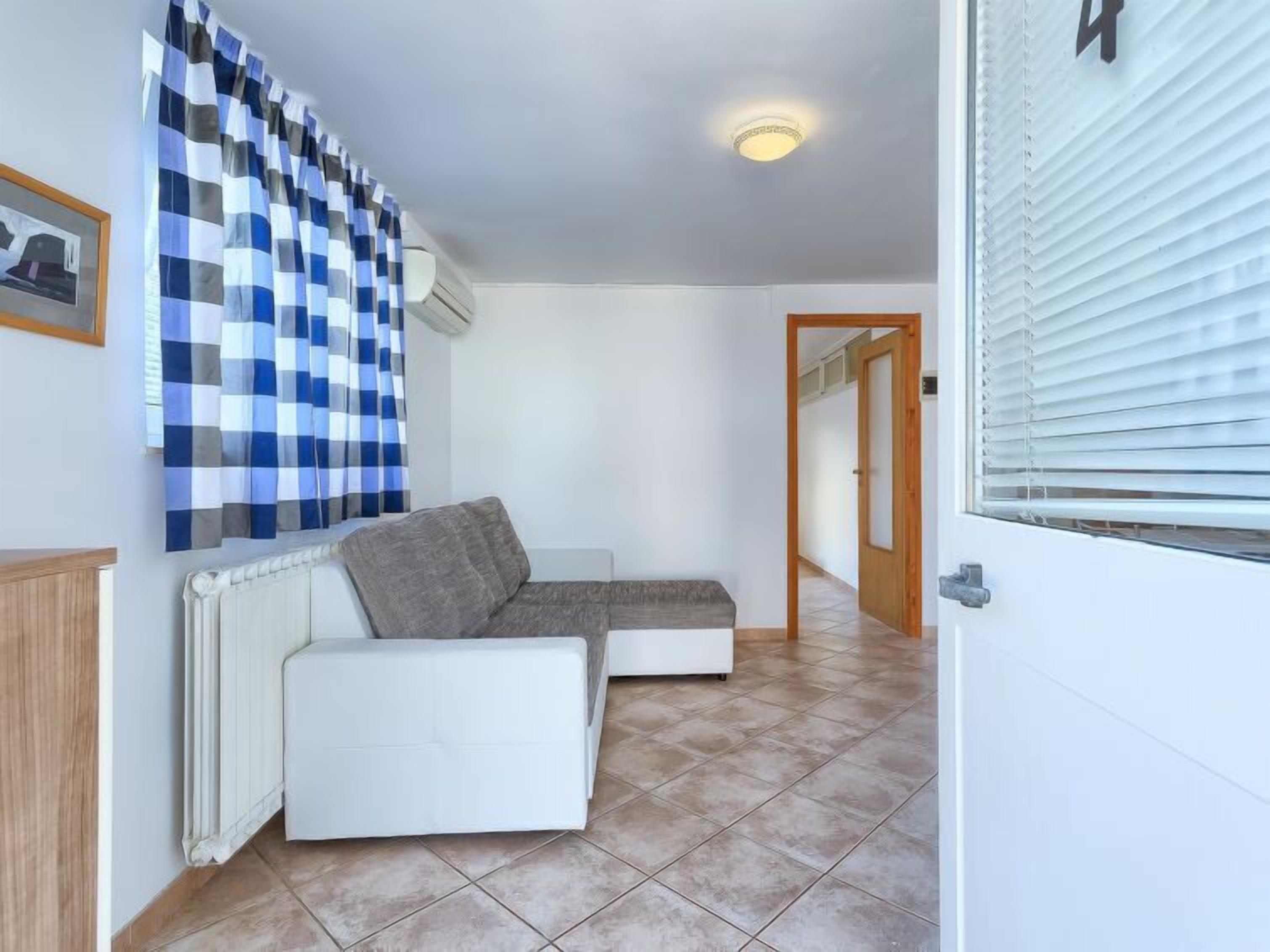A room with a white sofa, a checkered curtain, a radiator, and a door with a number '4' sign.