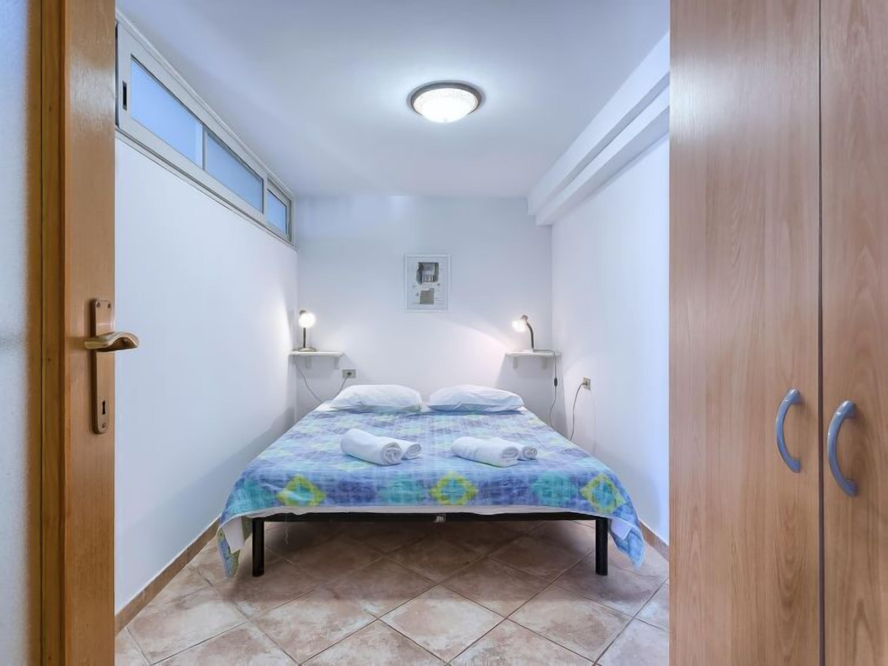 Une petite chambre à coucher, bien éclairée, avec un lit, des lampes de chevet et un luminaire au plafond.