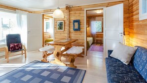 Interior acolhedor de uma cabana, com paredes de madeira, uma mesa de jantar, um sofá e uma cadeira.