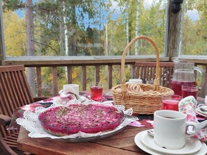 A wooden table with a glass pie, a wicker basket, and a pitcher of red beverage on a porch with a view of trees. - Jussinlahti, vaikon loma 6 by Interhome (Kaavi)
