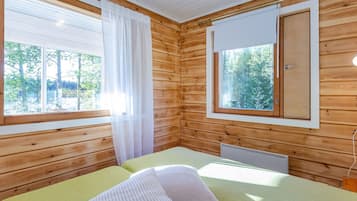 A cabin room with a bed, a window with a view of trees, and a small window with a door.