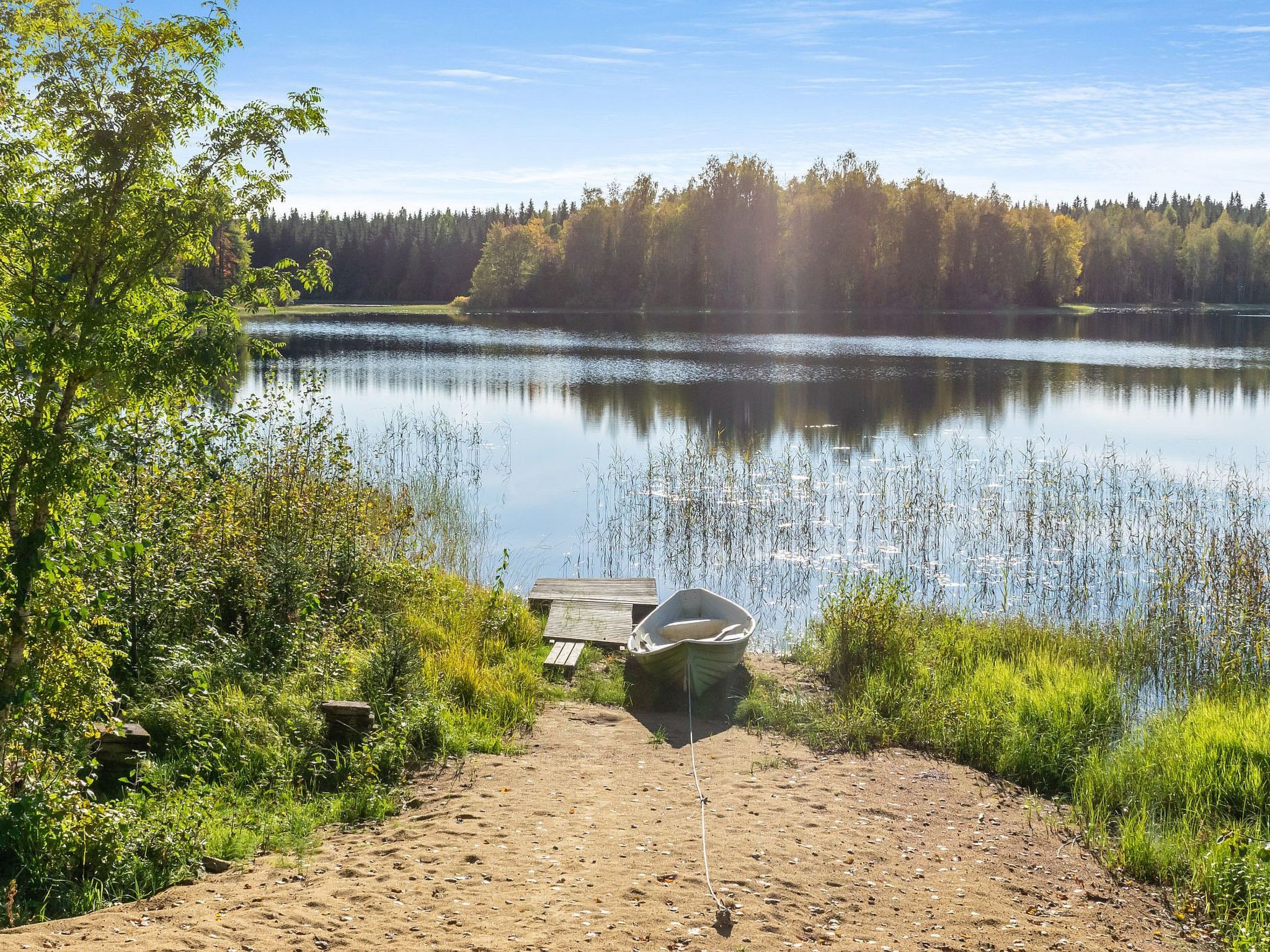 Une scène au bord d’un lac, avec une jetée en bois, un bateau et un petit abri.