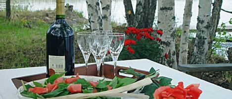 A table with a bottle of wine, glasses, a bowl of salad, and a rose.
