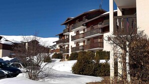 A multi-story hotel with balconies, a ski slope in the background, and parked cars. - Plein Soleil by Interhome (La Toussuire)