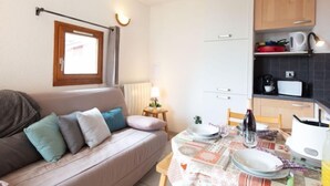 A compact living space with a sofa, a dining table set for two, and a kitchenette with cabinets and a microwave. - Plein Soleil by Interhome (La Toussuire)