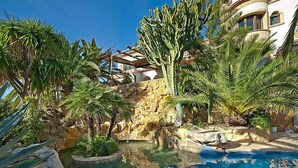 A pool surrounded by tropical plants and a stone wall. - St Anthony by Interhome (Jávea)
