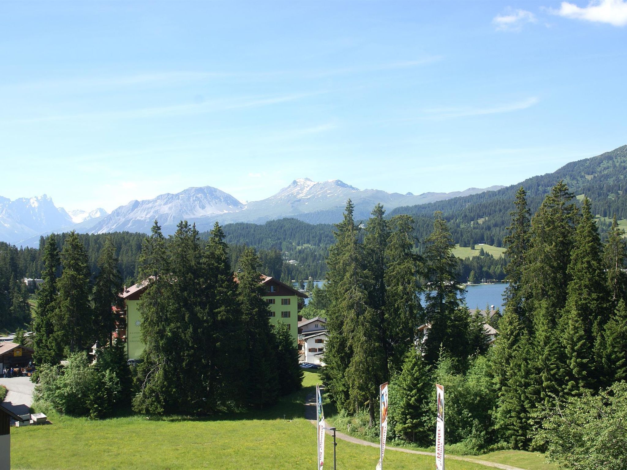 Paisagem montanhosa com um lago, casas e floresta densa.