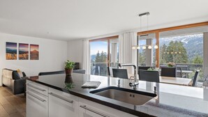 Een moderne keuken met een groot eiland, een eethoek met terrasmeubels en uitzicht op bergen.