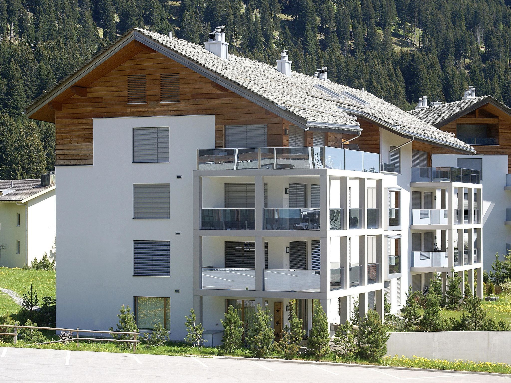 A modern multi-story building with balconies, large windows, and a sloped roof.