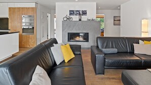 Een moderne woonkamer met een open haard, zwarte leren banken en een keukenhoek met inbouwapparatuur.