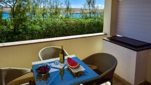 A balcony with wicker chairs, a table with a bottle, a bowl of cherries, and a watermelon slice. - Apartment Marija by Interhome (Pag/Dinjiška)