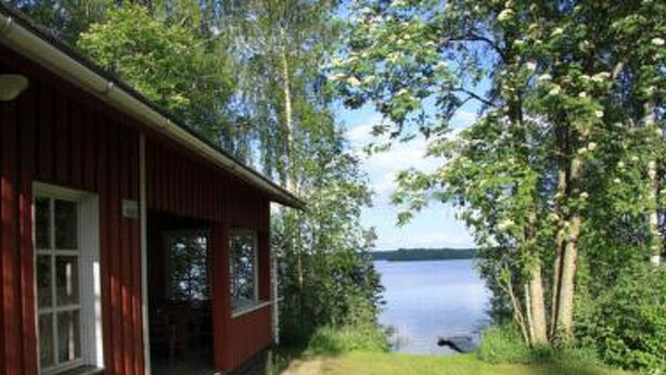 En træhytte med veranda, fri udsigt til søen, og en sti ned til vandet.