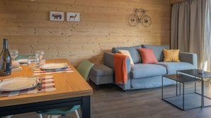 Ein modernes Wohnzimmer mit einer Holzvertäfelung, einer Couch, einem Esstisch gedeckt mit Tellern und Gläsern sowie einem an der Wand hängenden Fahrrad.
