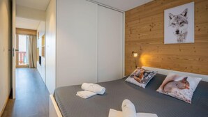 Ein Hotelzimmer mit einem Bett, einem hölzernen Kopfteil, einem Wandbild eines Wolfes und einem zur benachbarten Kammer führenden Gang.