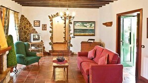 A cozy living room with a green armchair, a red sofa, and a tiled floor. There is a staircase leading to another level, a stone wall, and a painting of the ocean. - Camino La Candelaria by Interhome (La Orotava)