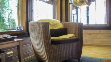 A wicker armchair with a fur throw and a pillow, positioned in a room with wooden walls and large windows.