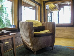 A wicker armchair with a fur throw and a pillow, positioned in a room with wooden walls and large windows.