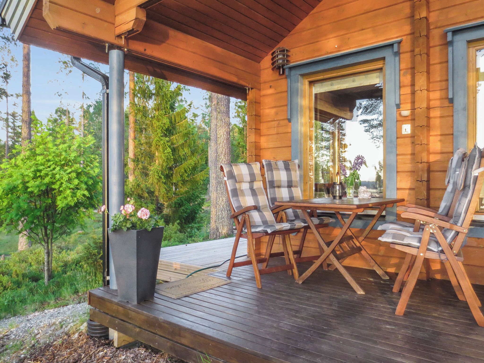 Une terrasse en bois avec une table et quatre chaises, entourée de verdure et d’arbres.
