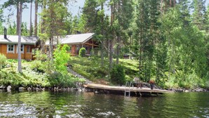 Une cabane avec un quai s’avançant dans un lac, entourée d’une forêt dense.