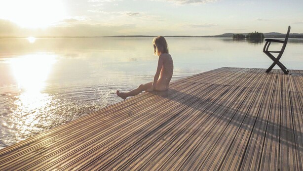 Une personne assise sur une jetée en bois, au bord d’un lac paisible, au coucher du soleil.