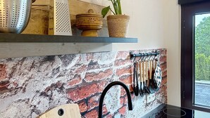 Una cocina con protector mural de ladrillo, un colgador para utensilios y una planta en maceta.