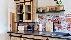 Una cocina con armarios de madera, salpicadero de ladrillo, encimera negra y una planta colgante.