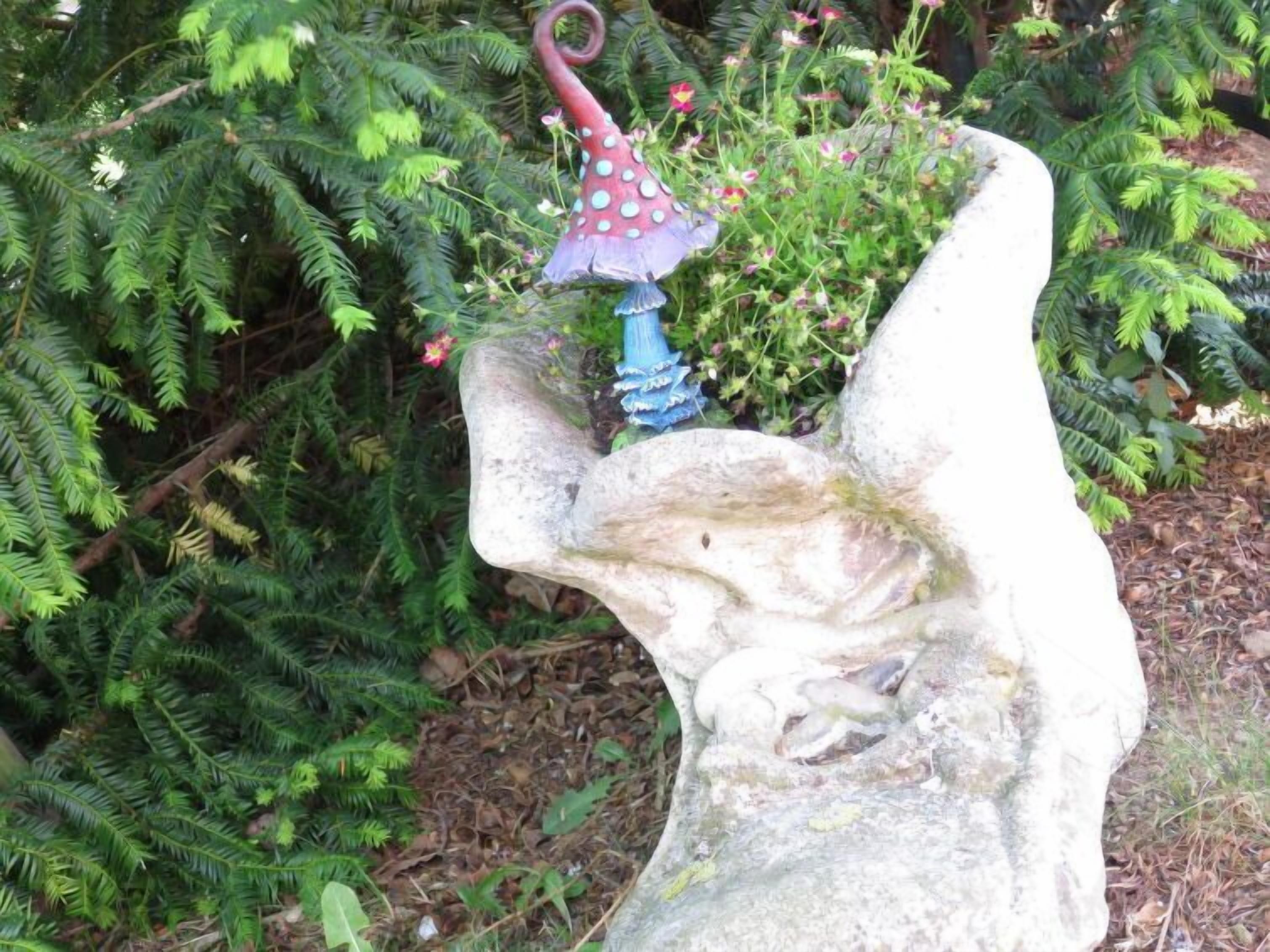 Una escultura de piedra de una mano sosteniendo un hongo con gorro rojo y tallo azul.