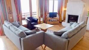 A living room with two grey sofas, a wooden coffee table, a black chair, a television, and a fireplace. - Le Bristol C54 by Interhome (Villars)