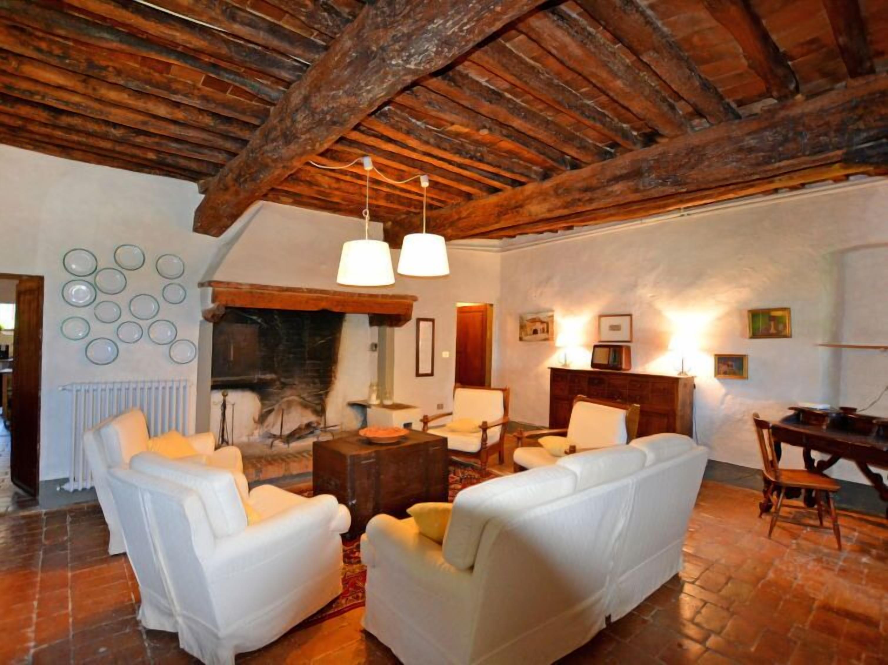 Una sala de estar acogedora con sofás de cuero blanco, chimenea y vigas de madera en el techo.