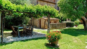 Un edificio in pietra con un patio giardino, una pergola ricoperta di piante rampicanti e un tavolo con sedie.