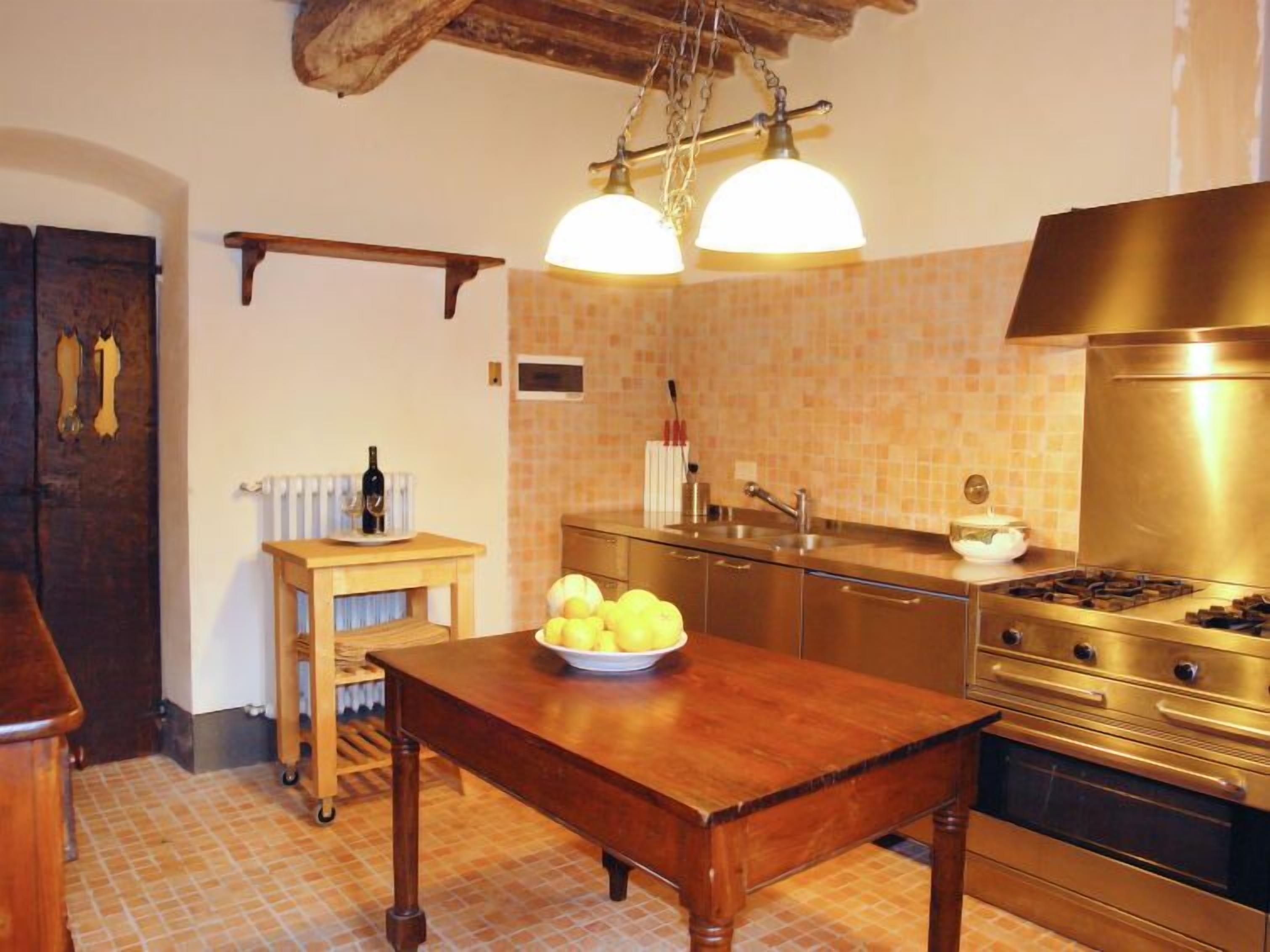 A kitchen with a wooden table, a bowl of lemons, a wine bottle, and a stove.