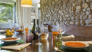 Un tavolo da pranzo apparecchiato con piatti, bicchieri e bottiglie, con una parete in pietra e una finestra sullo sfondo.