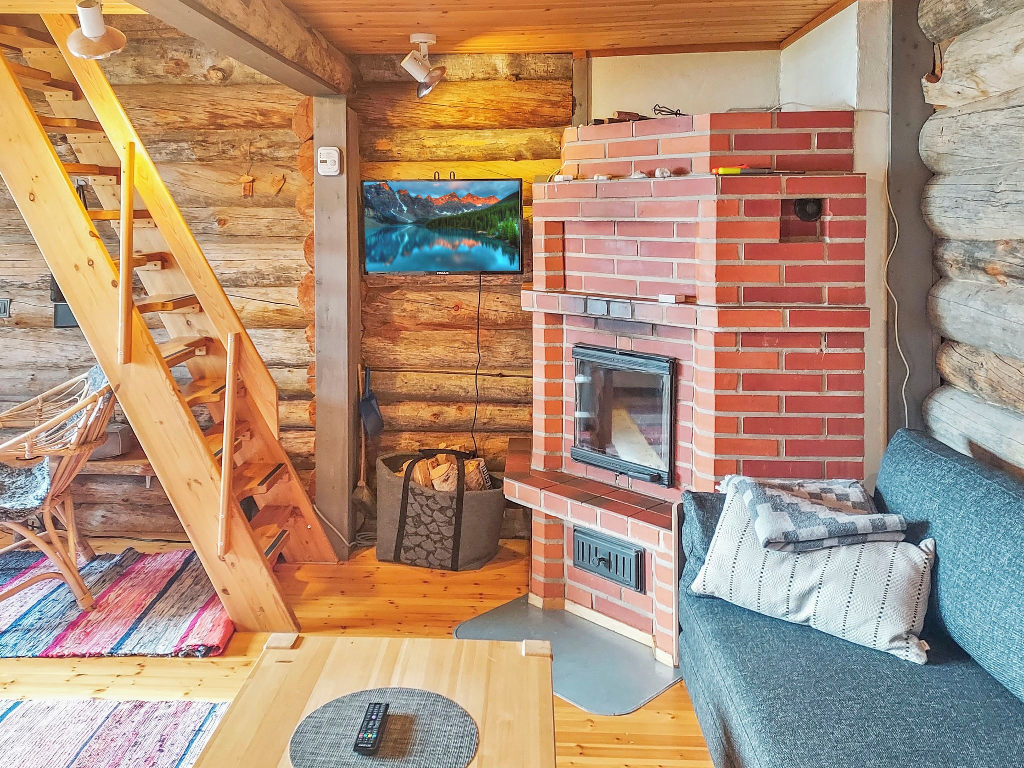 Ein gemütliches Blockhaus-Interieur mit einer Holztreppe, einem Kamin, einem Fernseher und einem Sofa.