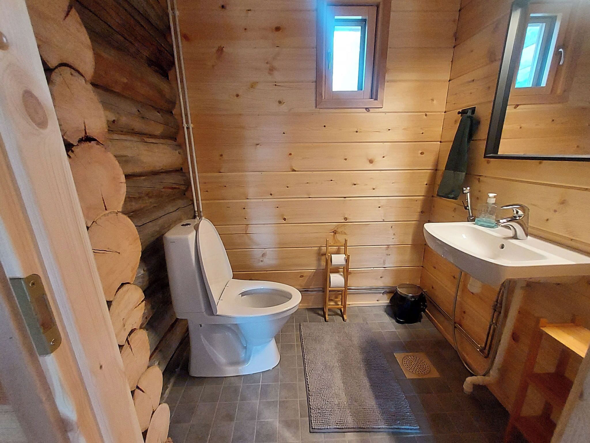 A wooden cabin bathroom with a toilet, sink, and a small window.