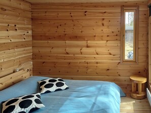 A wooden cabin room with a bed, pillows, a small stool, and a window. - Alakitkajärvi, takkusalmi by Interhome (Kuusamo)