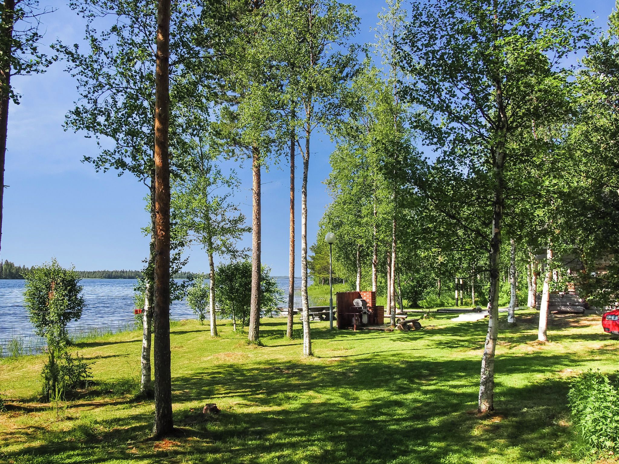 A lakeside campsite with picnic tables, a barbecue grill, and a small cabin.