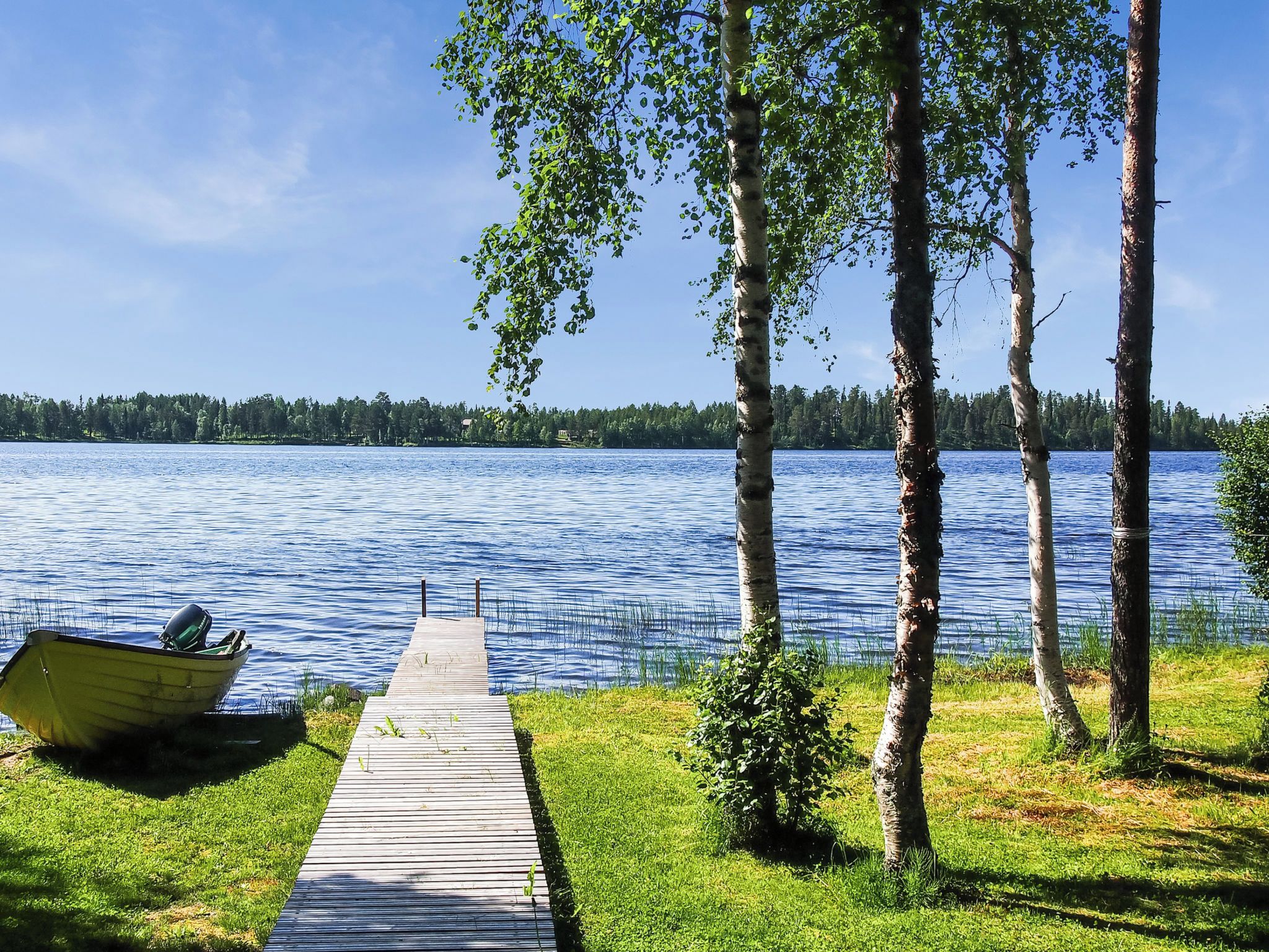 A wooden dock leading to a calm lake with a boat docked on the left.
