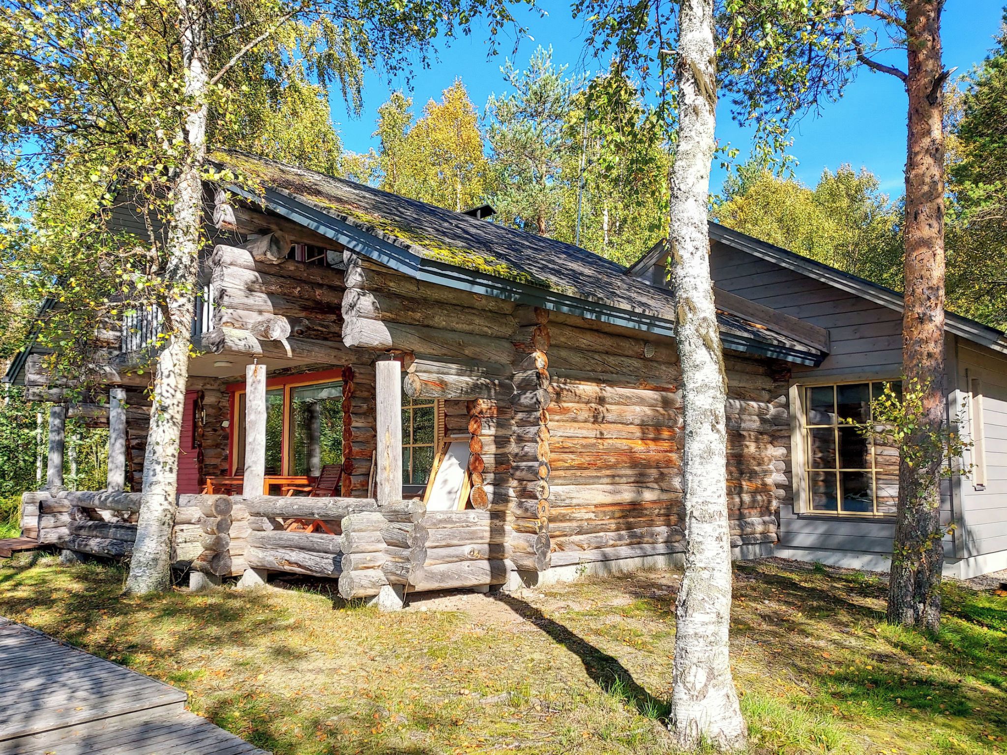A log cabin with a porch, wooden deck, and a large window.